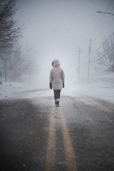 白天，穿着白大褂的女人在白雪覆盖的道路上行走